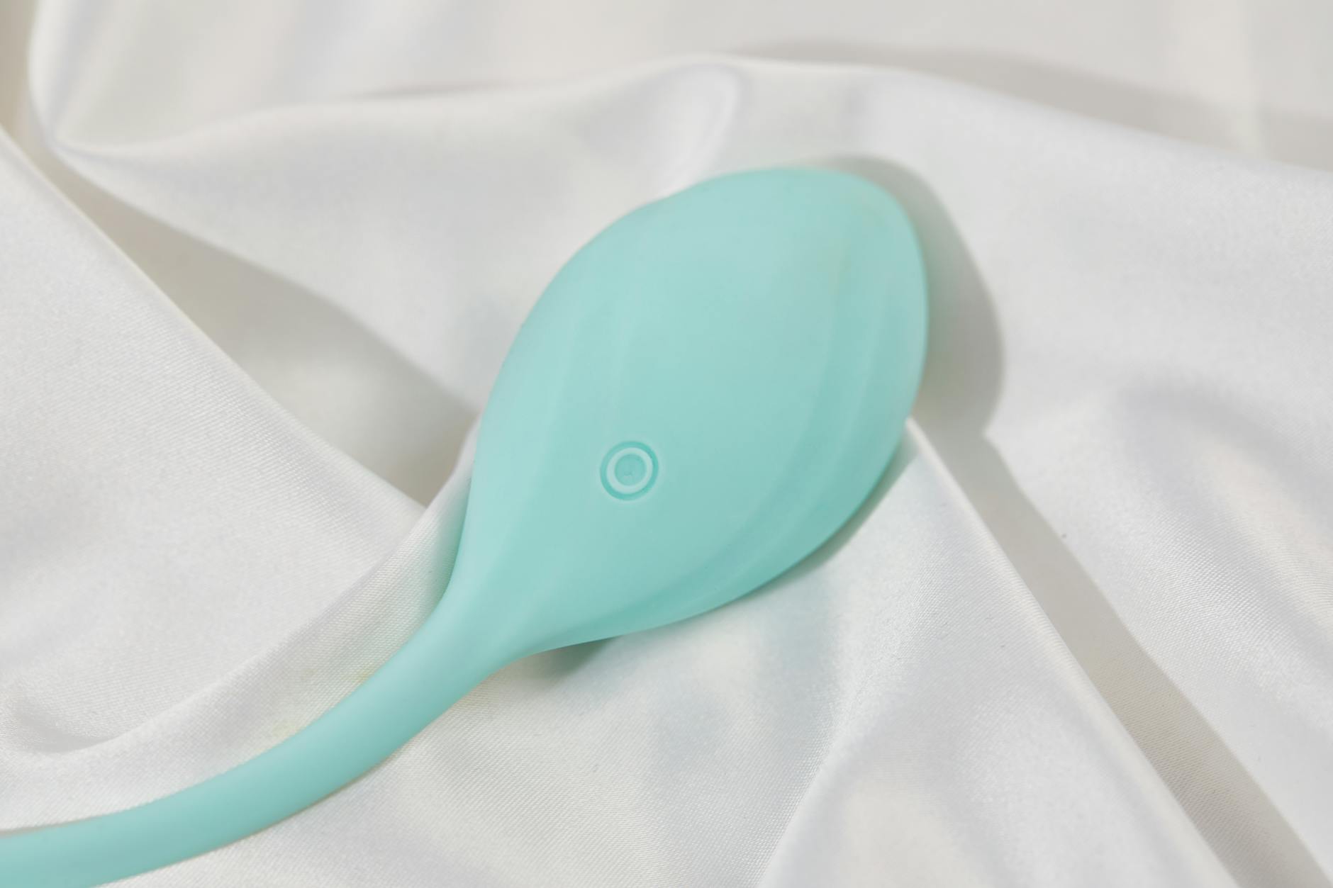A stylish teal vibrator on smooth white silk fabric, symbolizing calm self-care and relaxation