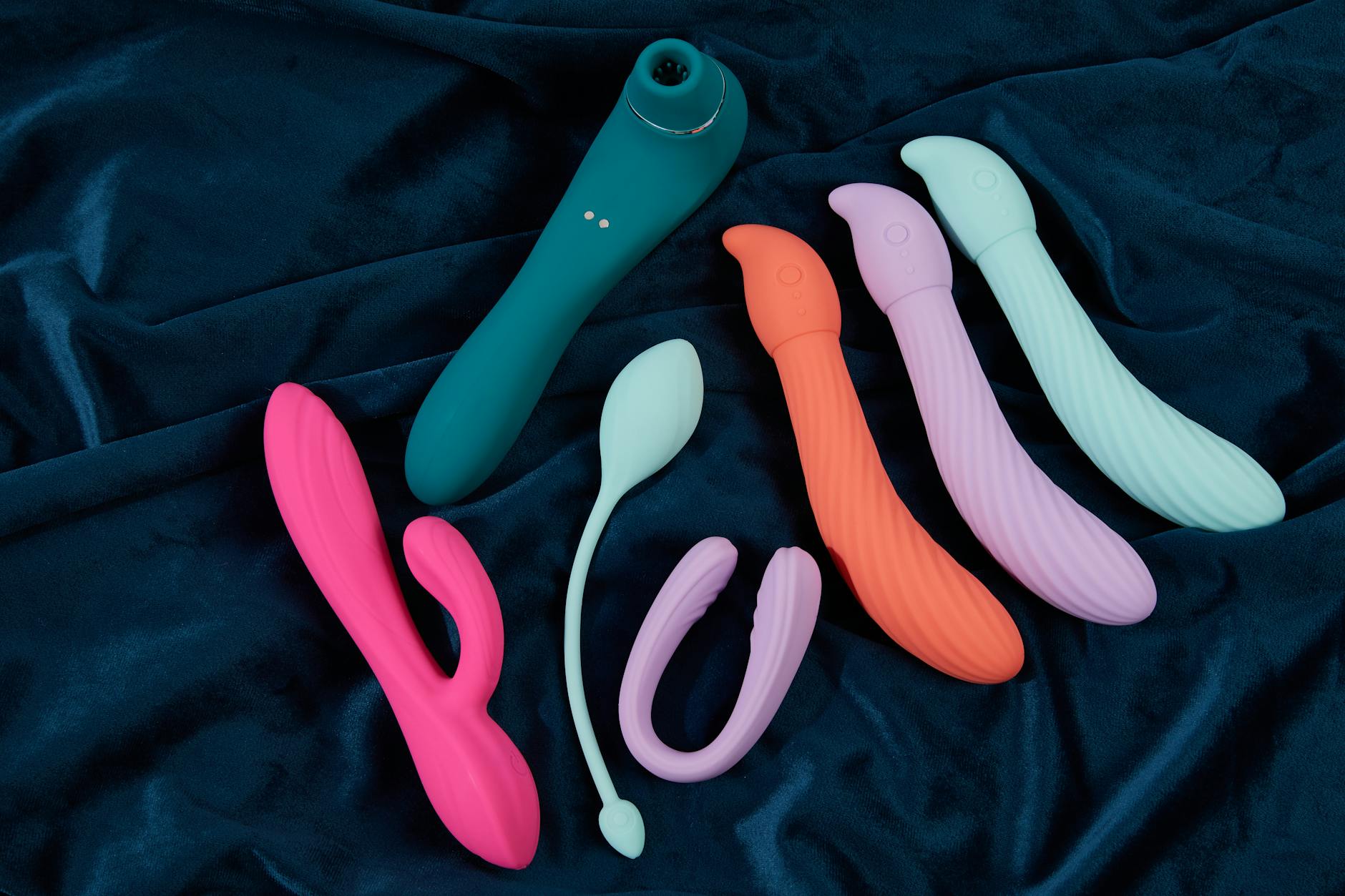 Person holding blue and pink silicone vibrators in a thoughtful pose