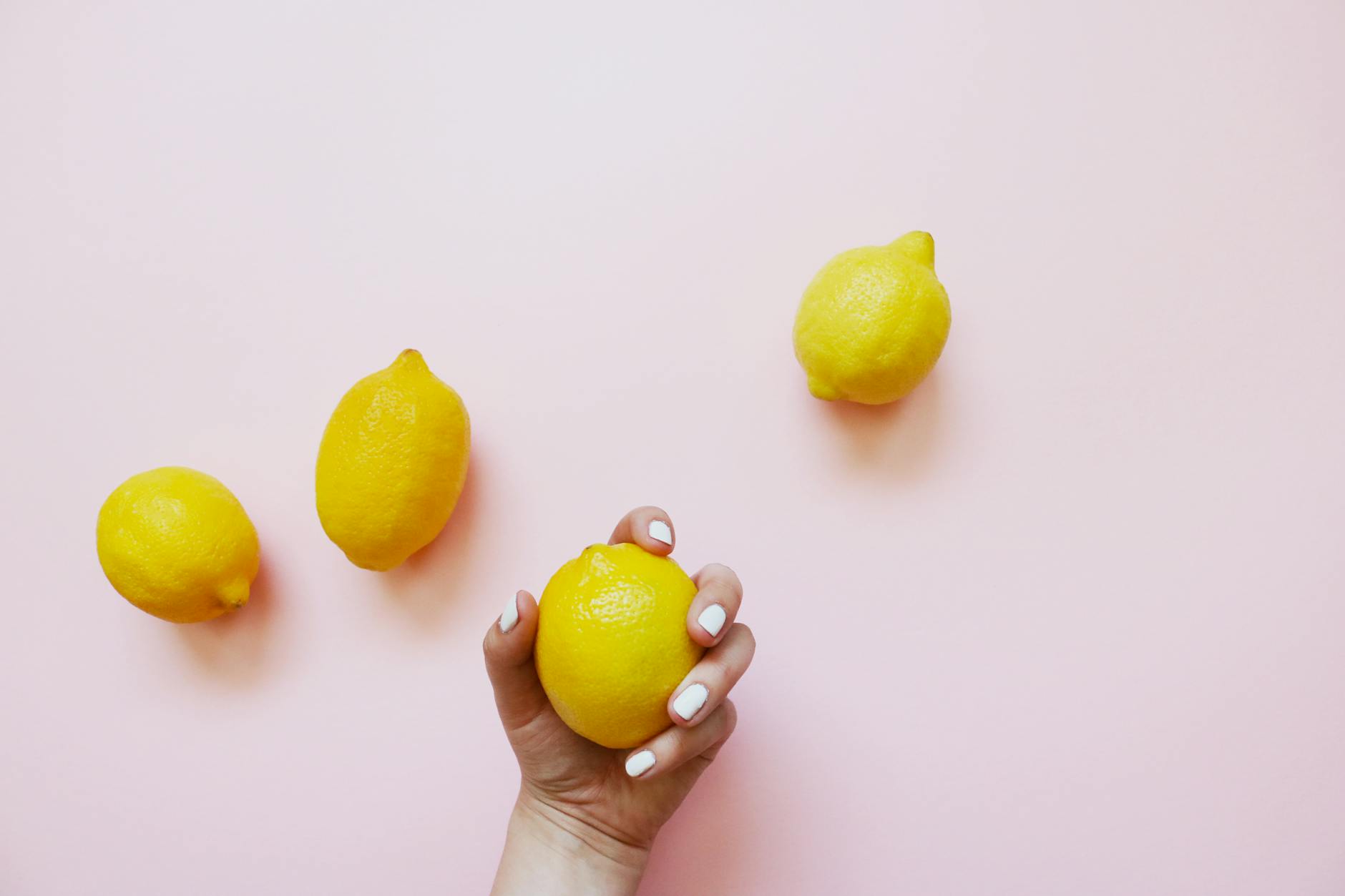 A hand holding a fresh lemon on soft pink background, symbolizing renewal and freshness