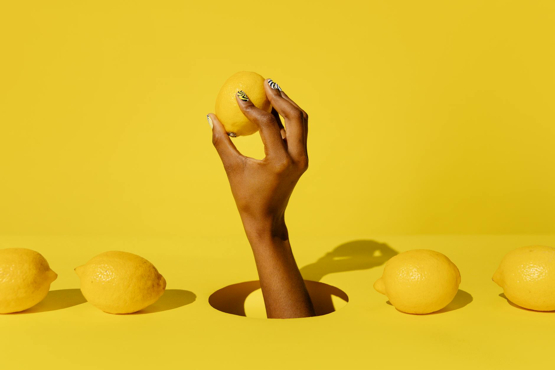 A hand holding a bright lemon against a vivid yellow background, symbolizing the citrus-inspired design of suction-based pleasure devices