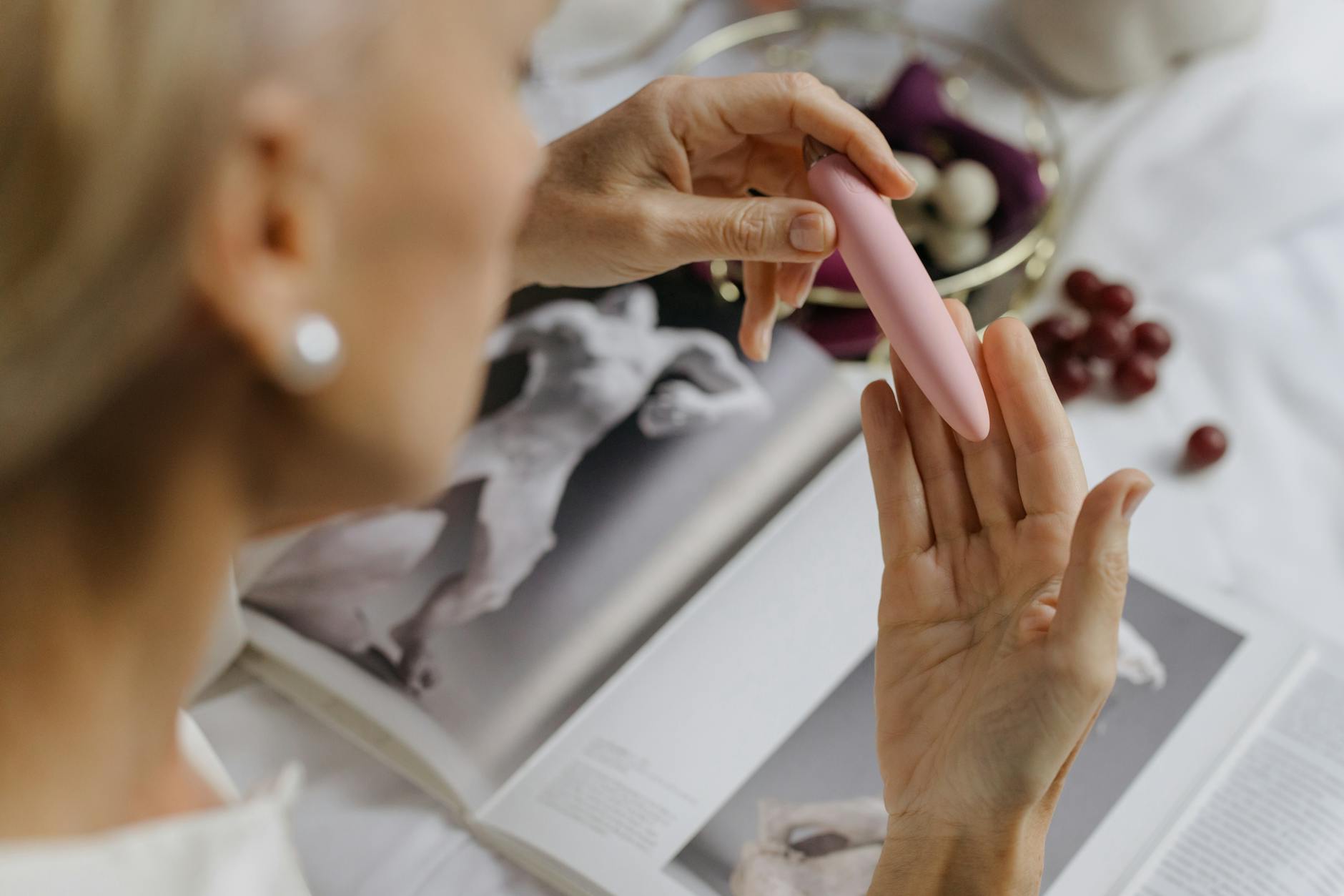 Close-up of a woman holding a pink vibrator with art books nearby, emphasizing intimacy and personal exploration.