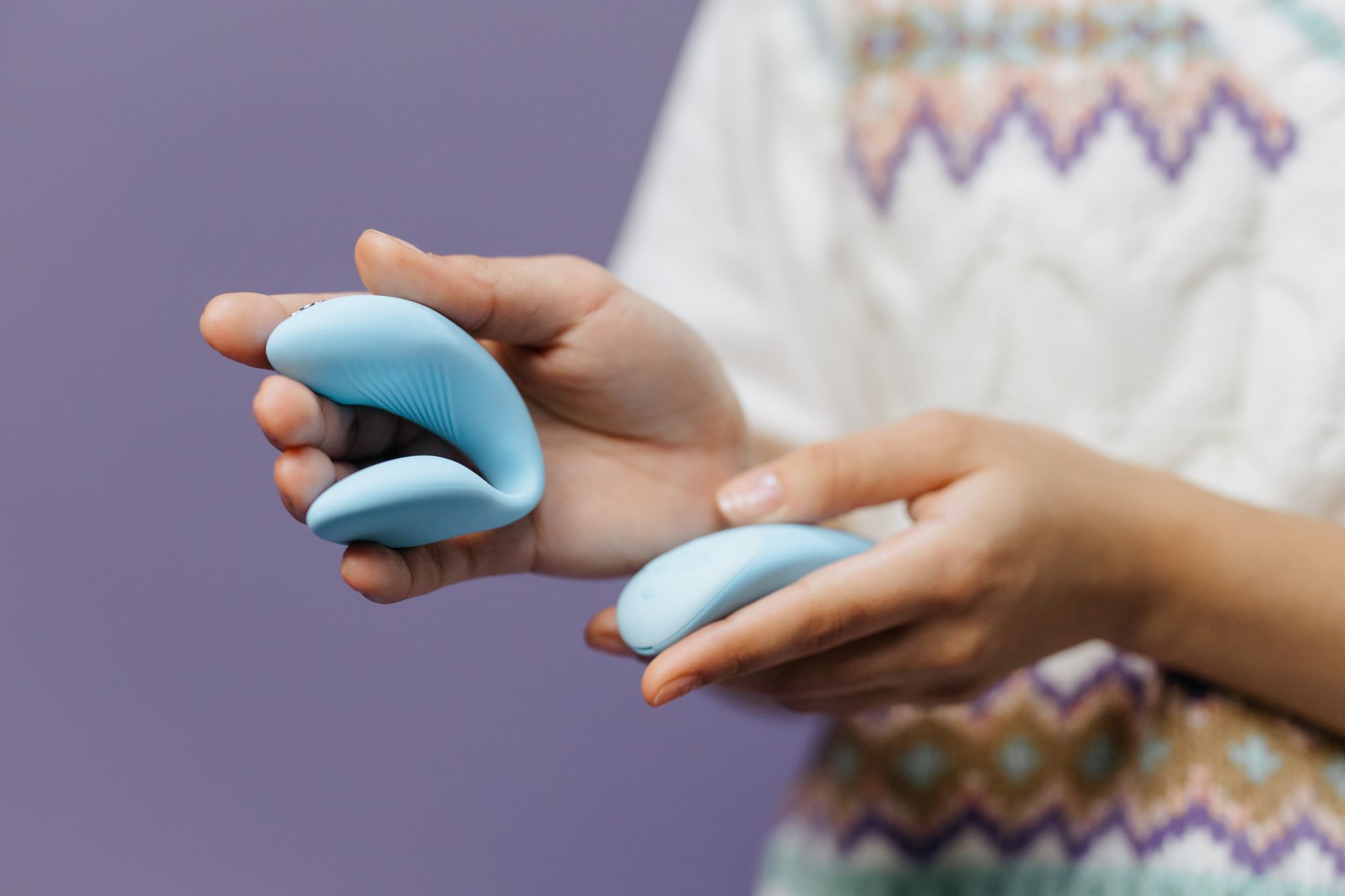Hands holding a lemon clitoral vibrator against a purple background, demonstrating proper technique