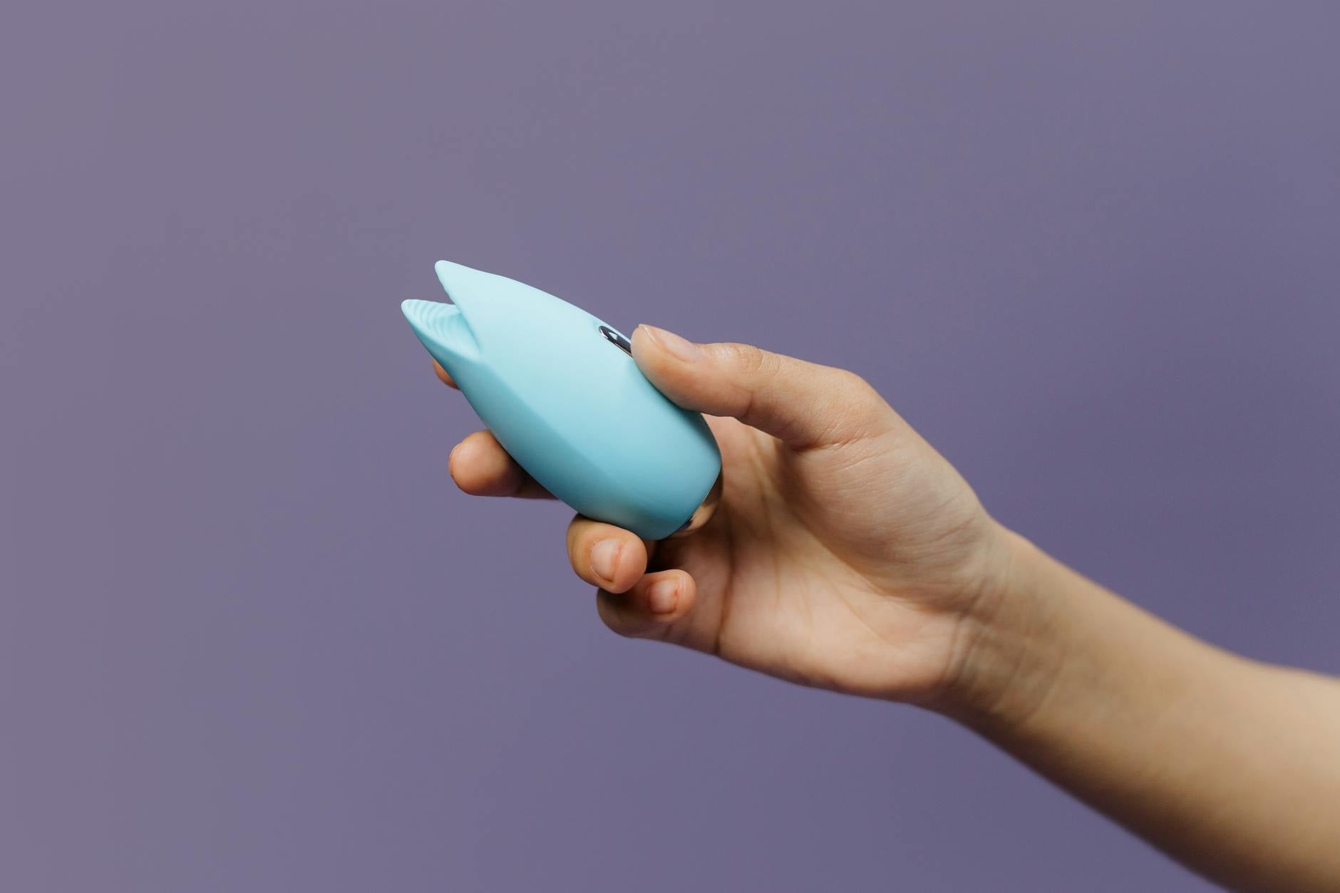 A blue silicone vibrator held in hand against a purple background, symbolizing self-care and intimate wellness during recovery