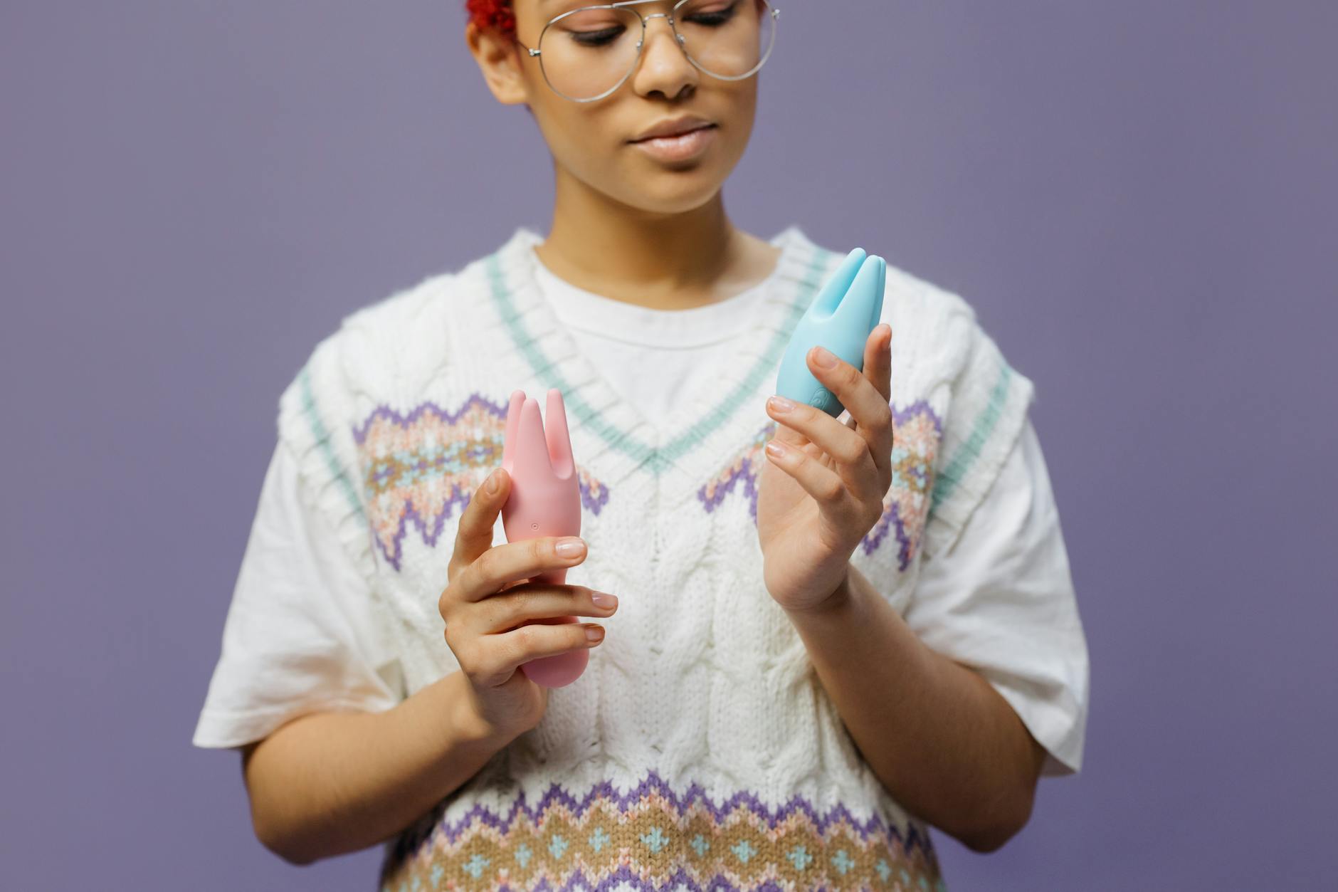 Woman holding colorful clitoral vibrators in contemplative pose against neutral background